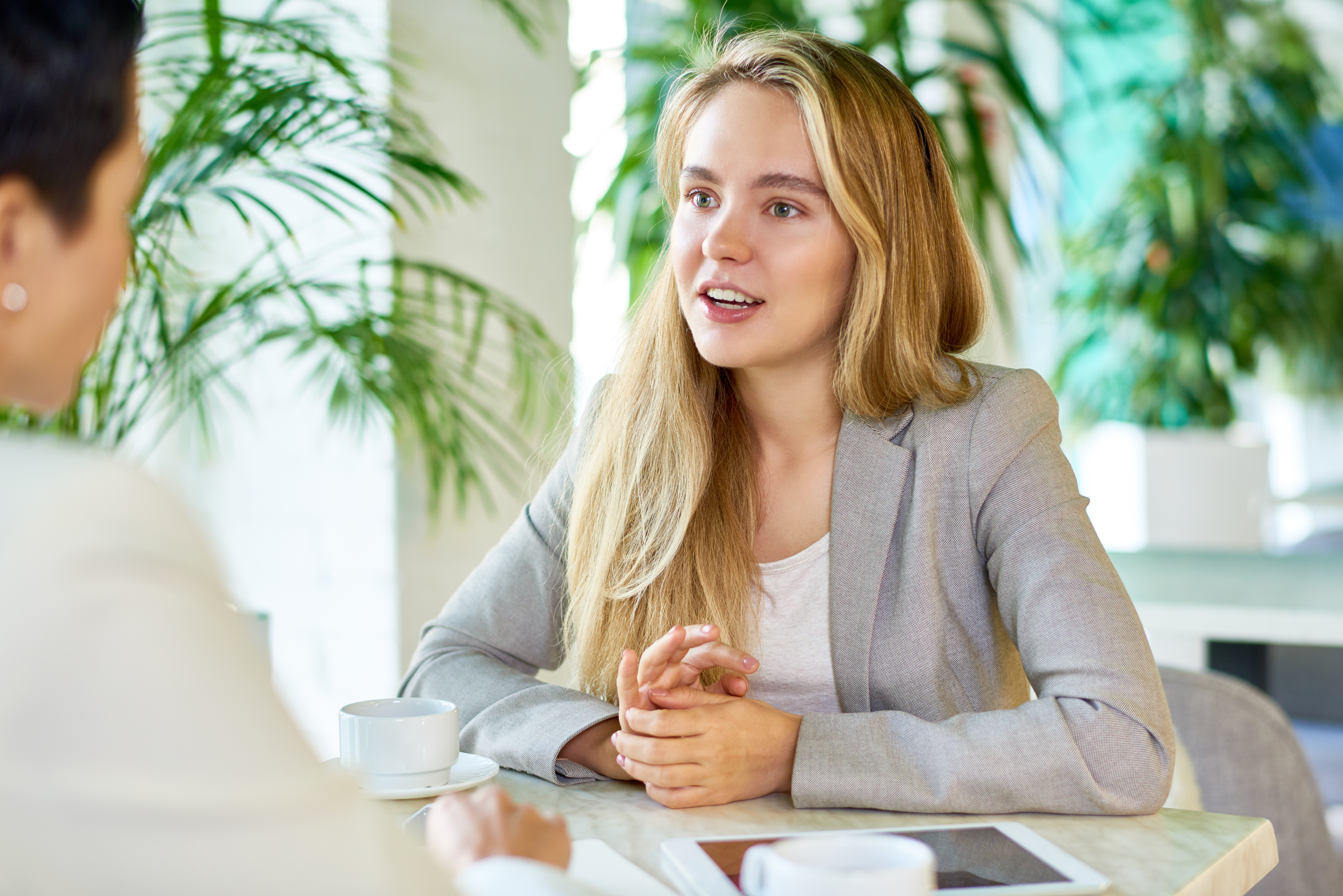 Woman at table with coffee speaking to another professional woman