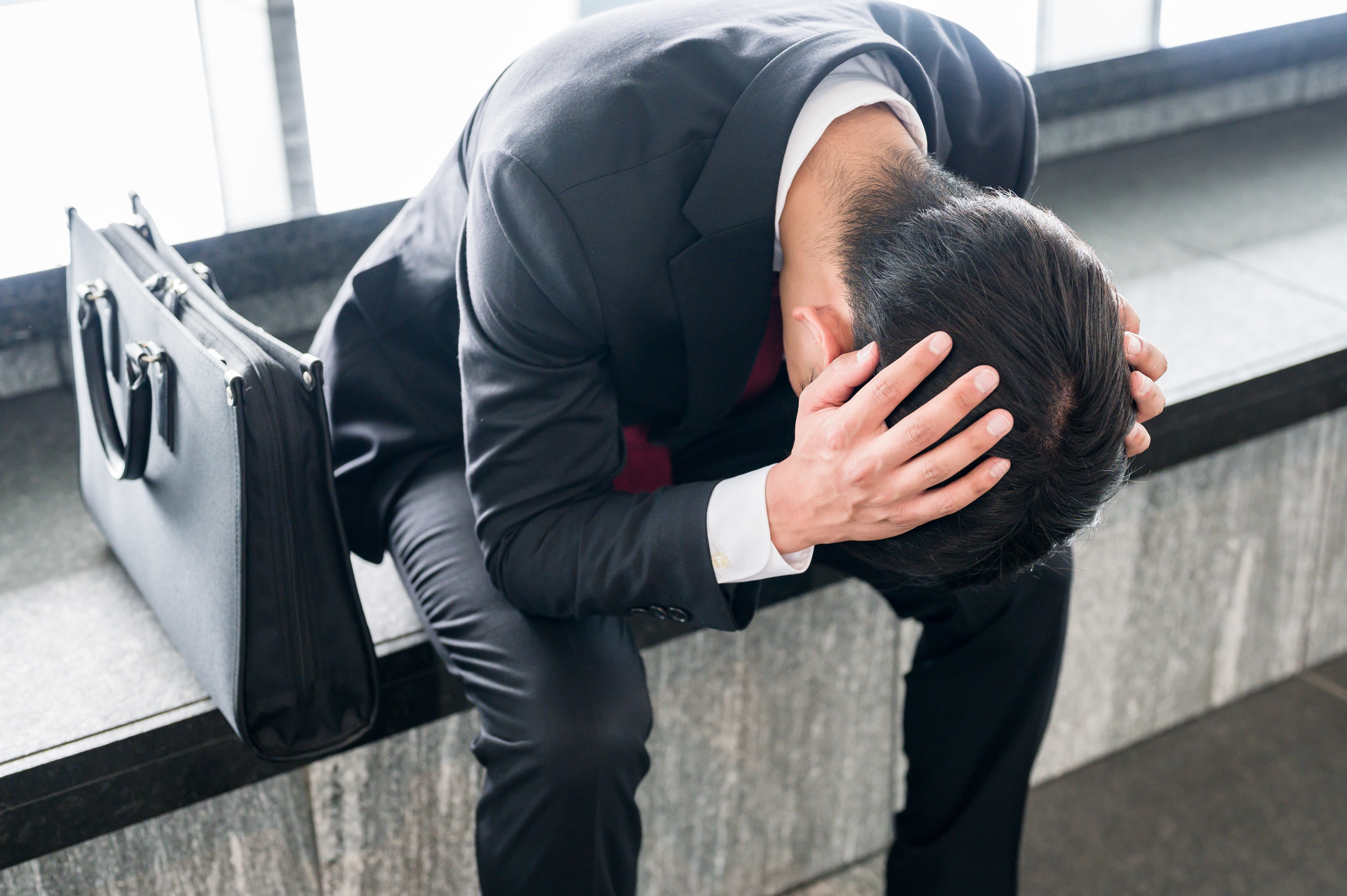 Male job hunter in business suit holding head down in hands